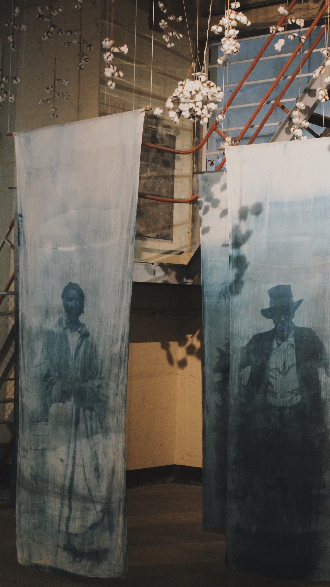 Portraits printed on blue fabric beneath hanging cotton branches